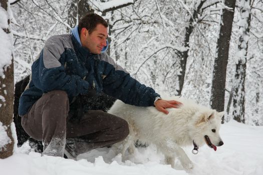 Man playing with Samoyed in the forest covered with snow