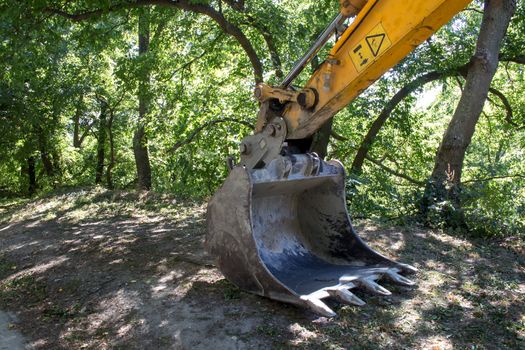 Part of the excavator in the country. Intense sunlight, green trees in the background.