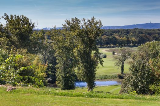 Nature in the late summer. Green grass, small lake and trees around. Mountain in the background together with a silhouette of Slovakia capital, Bratislava.