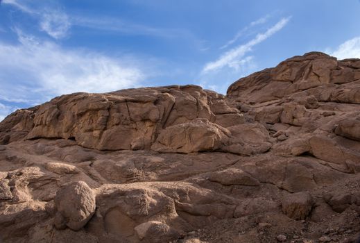 Landscape in the desert in Egypt. Small rocky hills. Blue sky with white clouds.
