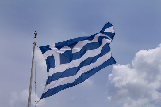 Greek flag blowing in the wind. Cloudy sky in the background.