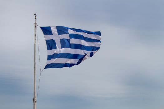 Greek flag blowing in the wind. Cloudy sky in the background.