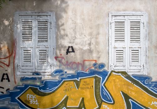 Old windows with a white shutters. Wall of the house with graffiti tags. Athens, Greece.