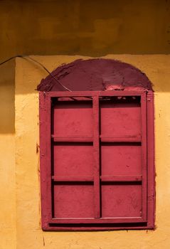 Fully red painted window with a grid. Yellow facade of the house.