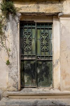 Facade of an old house. Entrance green iron door with a heart design grid. Plant in the corner on the wall. Athens in Greece.