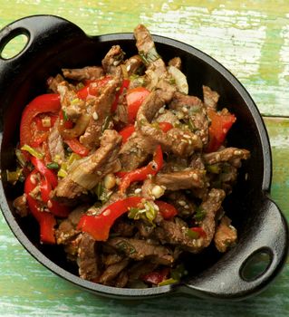 Delicious Beef Stir-fry with Sliced Red Bell Pepper, Leek and Sesame Seeds in Black Cast Iron closeup on Wooden background