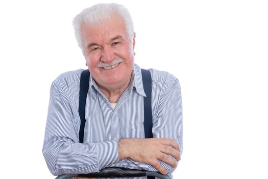 Cute senior man with mustache in white striped shirt and blue suspenders with joyful expression and folded arms over white background