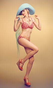 Sexy PinUp woman in fashion red polka dots swimsuit, blue hat, beach slim body. Playful blonde girl in bikini smiling. Summer holiday, sea vacation. Yellow, vintage toned, unusual creative provocative