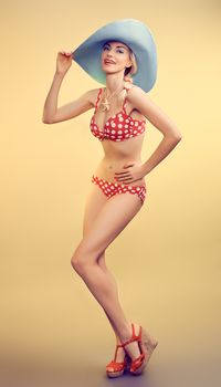 Sexy PinUp woman in fashion red polka dots swimsuit, blue hat, beach slim body. Playful blonde sensual girl in bikini. Summer holiday, sea vacation. Yellow, vintage toned, unusual creative provocative