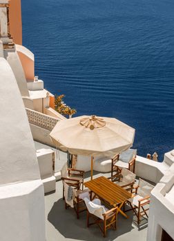 view from cliff onto terrace with table and chairs under umbrella in Oia Santorini