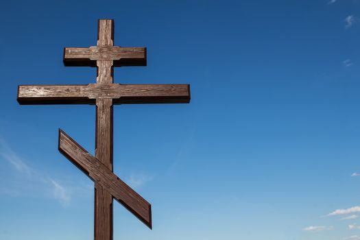 Wooden symbol: double cross. Blue sky in the background, several small white clouds.