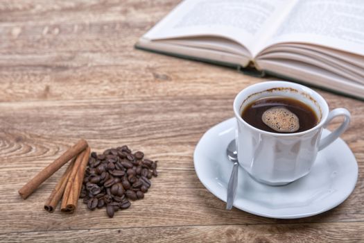 A cup of coffee and cinnamon with a book on a wooden background