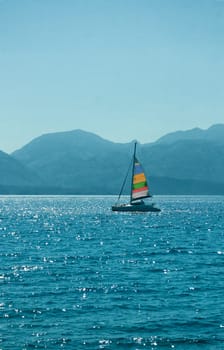 sailing boat with a colorful sail sails on a background of mountains in the haze on a sunny day