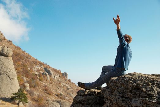 Man gesturing with raised arms with rocks landscape background