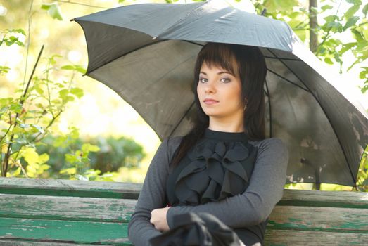 Portrait of beautiful girl with umbrella sitting in the park