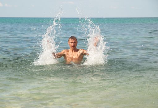 Happy man in the tropical sea with splashes