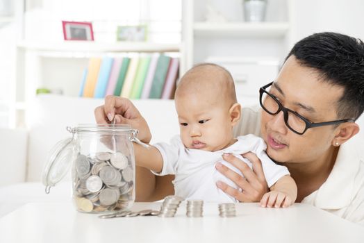 Asian family lifestyle at home. Father and baby putting coins into money jar, financial planning concept.