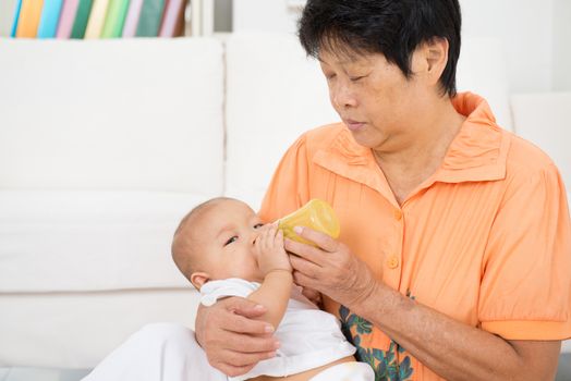 Babysitter taking care baby at home. Feeding solid food fruit puree with bottle.