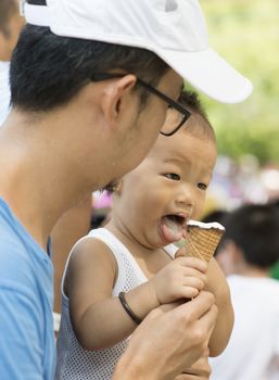 Asian father and child are eating ice creams on summer holidays. Candid family photo.