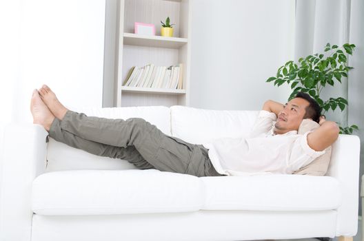 May guy resting and daydreaming at home. Asian handsome man relaxed and lying on sofa indoor. 