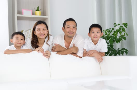 Asian family posing behind sofa.