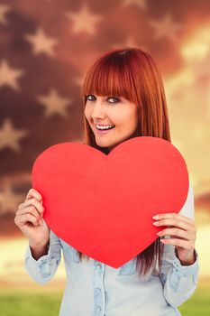 Attractive hipster woman behind a red heart against american flag rippling over grassy landscape