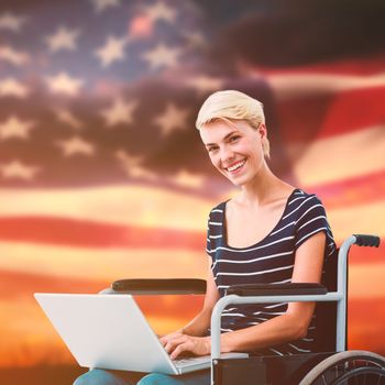 Woman in wheelchair using computer against digitally generated american flag rippling over grass
