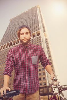 Hipster with bicycle against fence against skyscraper