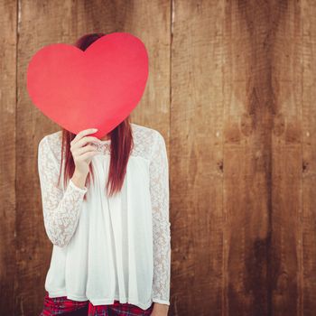 Smiling hipster woman behind a big red heart against weathered oak floor boards background