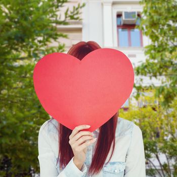 Attractive hipster woman behind a red heart against low angle view of city building