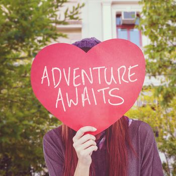 Hipster woman behind a red heart against low angle view of city building