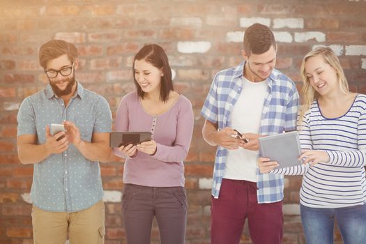 Smiling business people using electronic gadgets  against brick wall