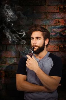 Confident hipster smoking pipe against texture of bricks wall