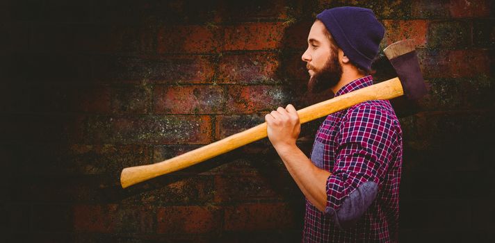 Side view of hipster with axe on shoulder against texture of bricks wall