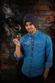 Portrait of hipster smiling while holding smoking pipe against texture of bricks wall