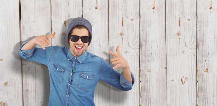 Happy hipster showing rock and roll hand sign against wooden background
