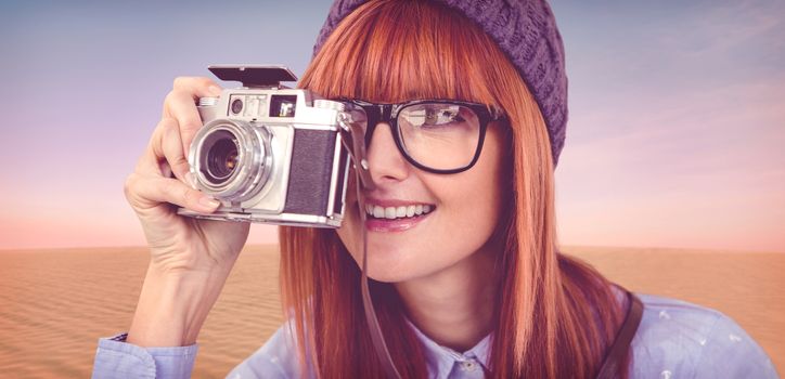 Smiling hipster woman taking pictures with a retro camera against desert scene