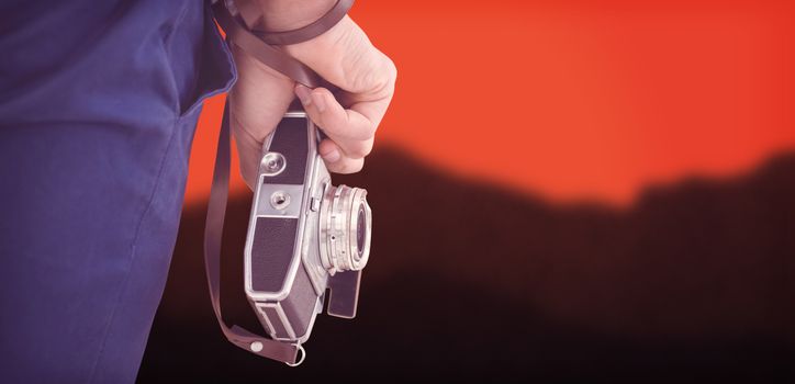 Cropped image of hipster holding camera against blurred mountains