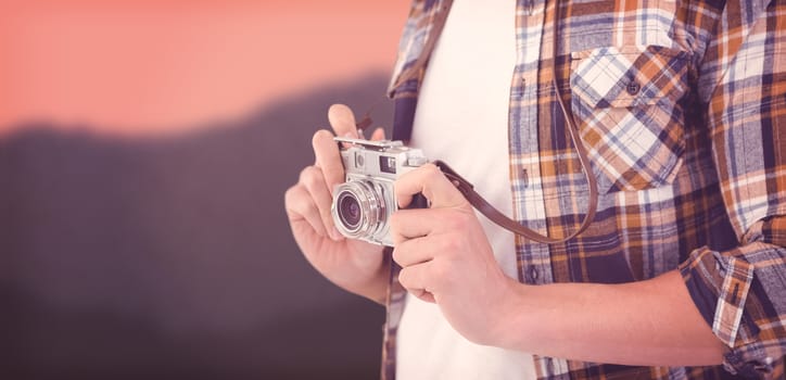 Mid section of hipster holding camera against blurred mountains