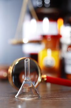 Chemical funnel near magnifying glass against blurred background with flasks