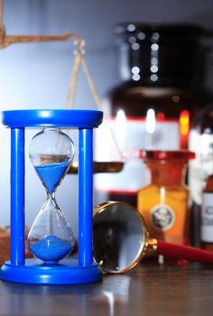 Blue hourglass against flasks near weight scale and magnifying glass