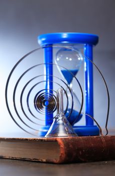 Education concept. Blue hourglass on old book near metal spiral