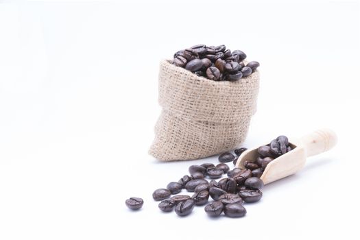 Coffee beans in a wooden scoop and spilling out from a hessian bag, over white background.