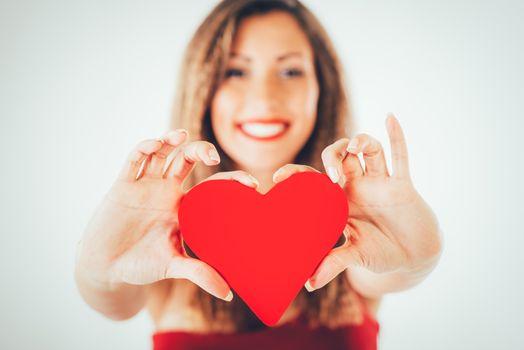 Close-up of a beautiful smiling girl holding a red heart. Selective focus. Focus on the heart.