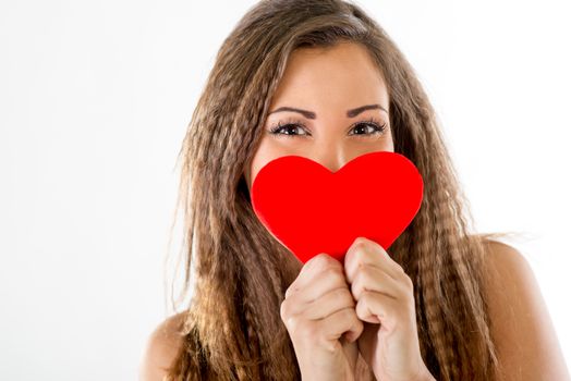 Beautiful smiling girl hiding behind a red heart. Looking at camera.