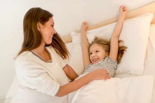 Happy attentive mother waking up her daughter at morning.