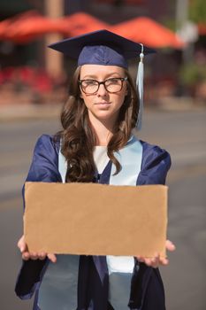 Graduate in blue gown holding a blank cardboard sign