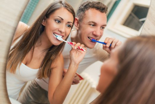 Portrait of a beautiful young happy couple brushing teeth in front of their bathroom mirror. Selective focus.