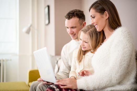 Beautiful young smiling family relaxing on sofa at living room while using laptop.