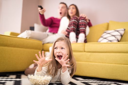 Beautiful young family watching a scary movie at living room. Selective focus.